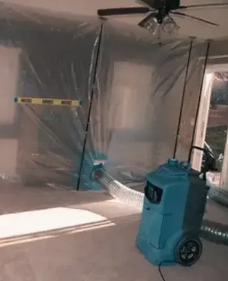 A dehumidifier drying a room sealed off with plastic containment during a water damage job