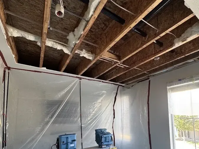 A ceiling opened to the joists with a dehumidifier running inside plastic containment