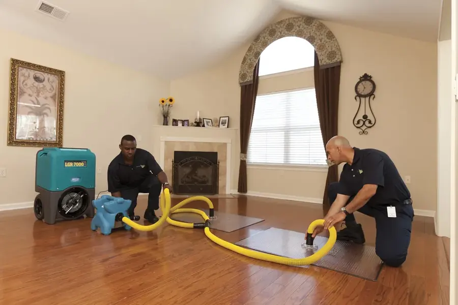 Two technicians setting up a dehumidifier and drying mats on a wet hardwood floor