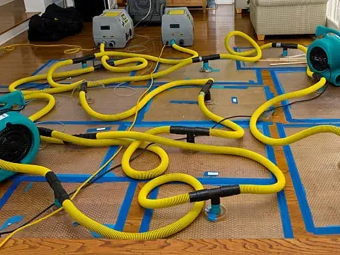 Drying panels and air movers taped down over a wet wood floor